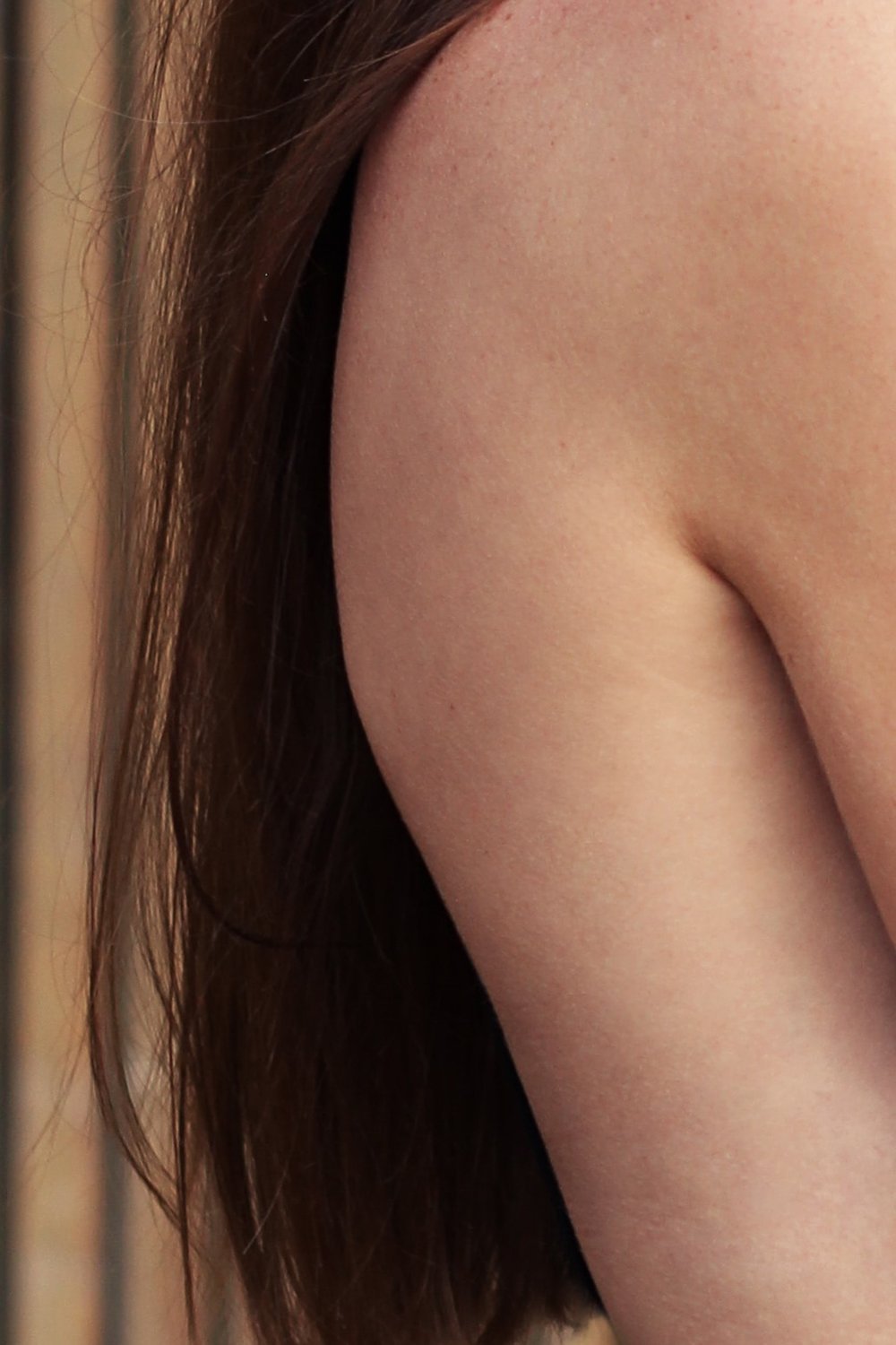 Close-up of a woman's bare shoulder and upper arm with long brown hair falling across it, soft natural lighting.